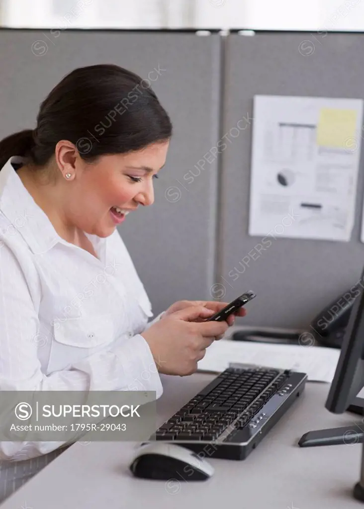Businesswoman texting at her desk in cubicle