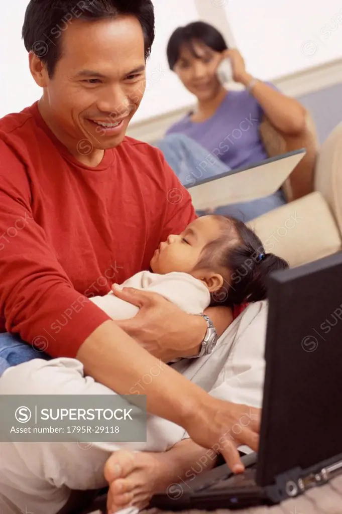 Father holding his sleeping daughter while typing
