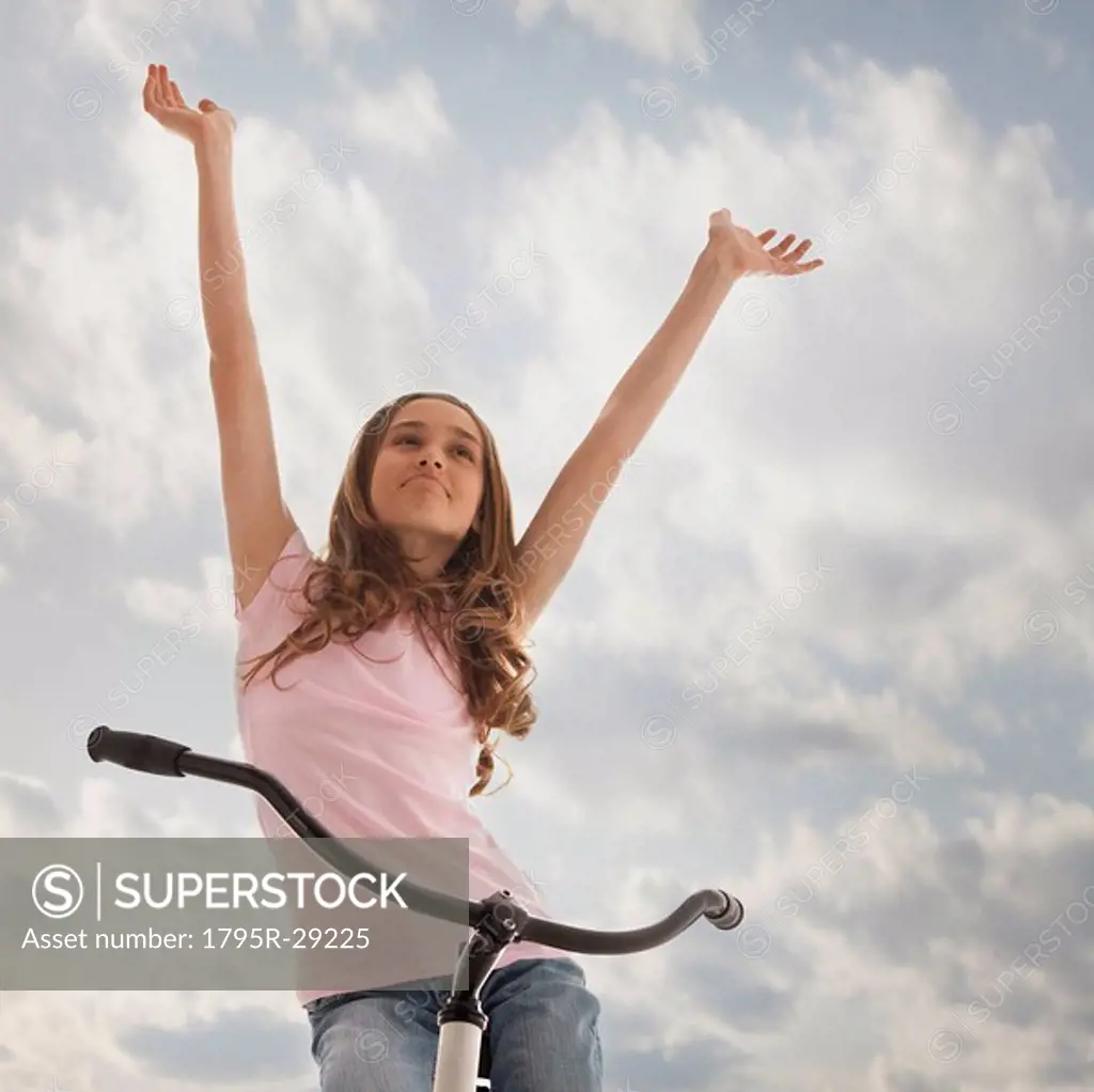 Pretty teenage girl with her arms raised while sitting on bike