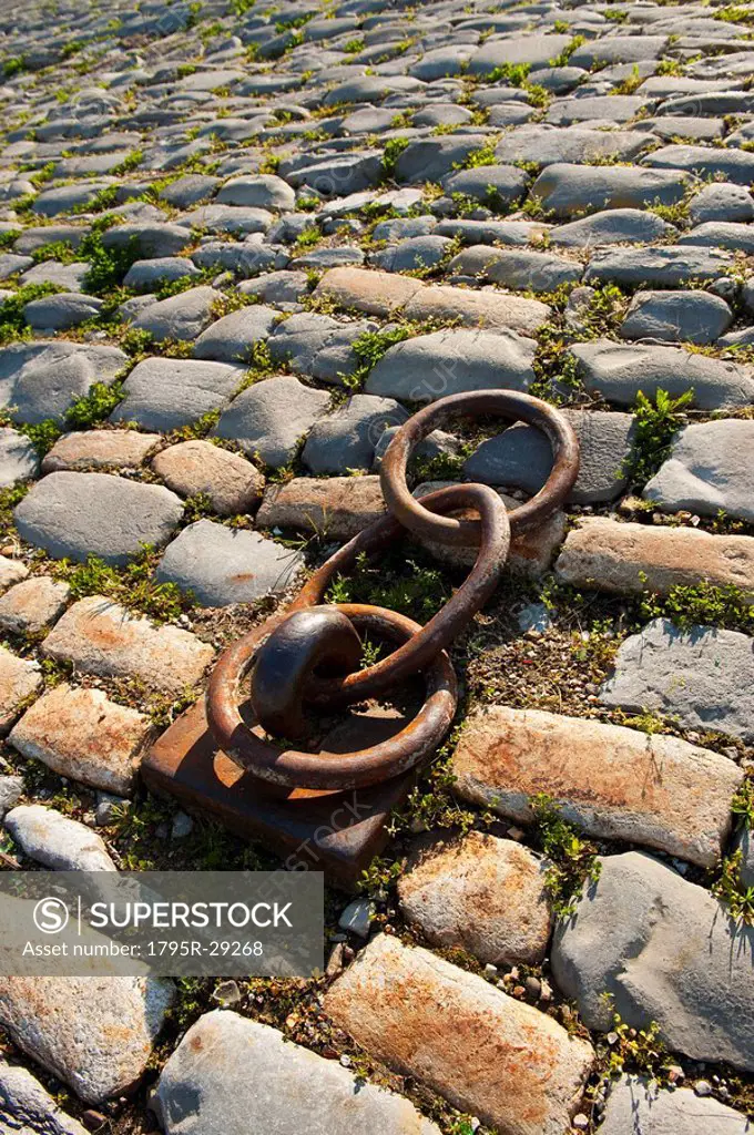 Rusty chain anchored to the ground amongst cobblestones