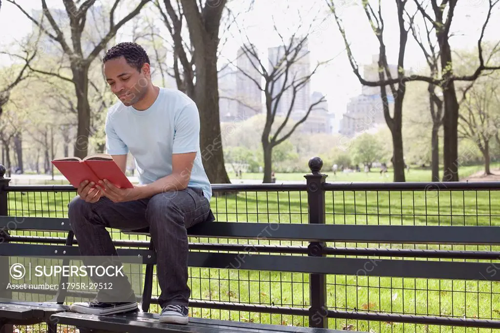 Man sitting on bench reading book in Central Park