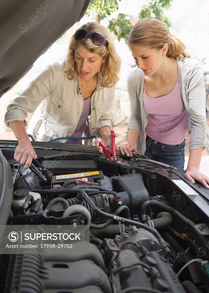Mother and daughter looking under hood of car