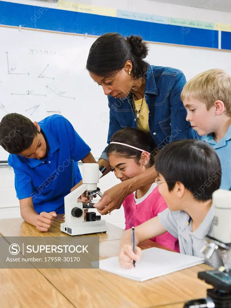 Teacher helping students use microscope in science lab