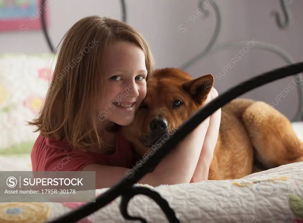 Young girl hugging dog on bed