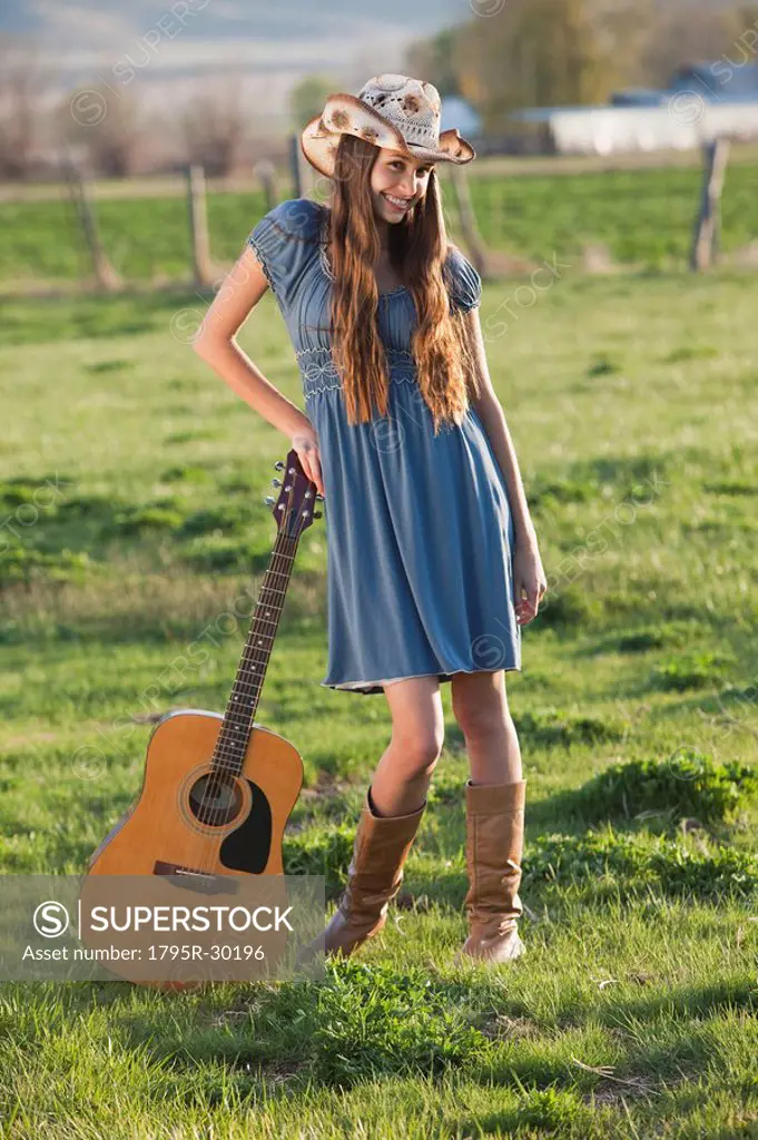Long haired cowgirl holding guitar in field