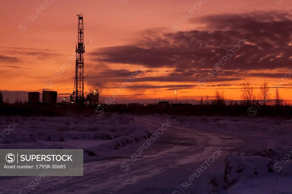 Snowy road at dusk with oil drilling rig in background