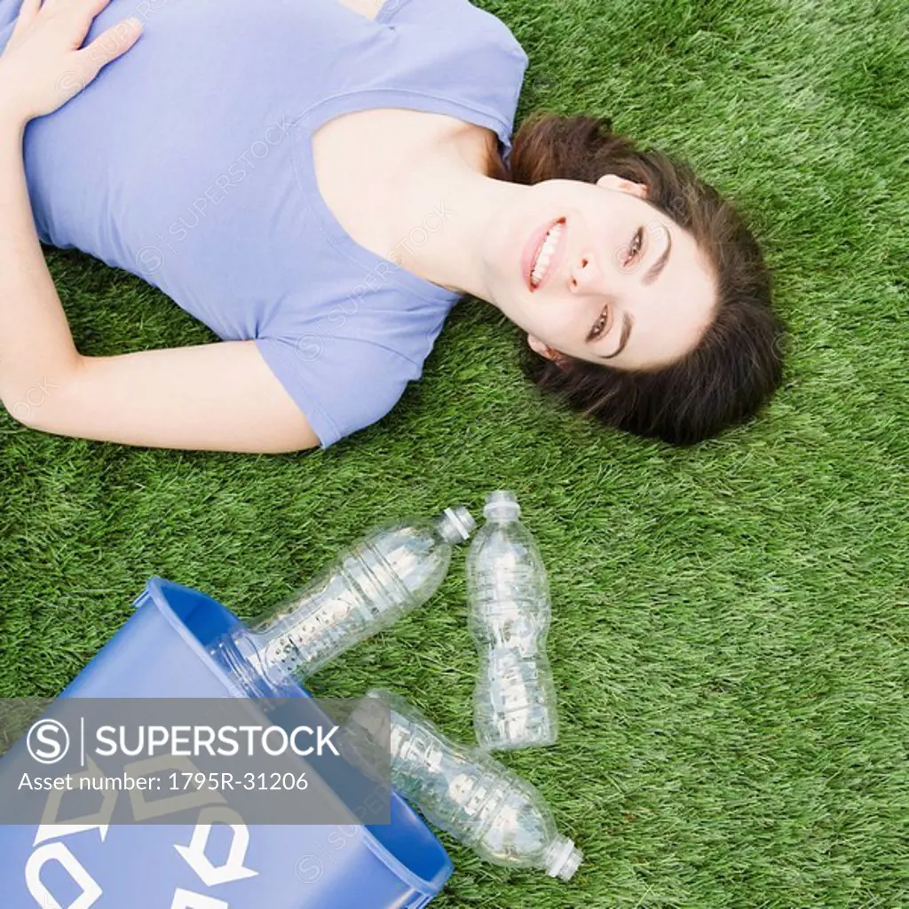 Woman lying on grass beside recycling bin
