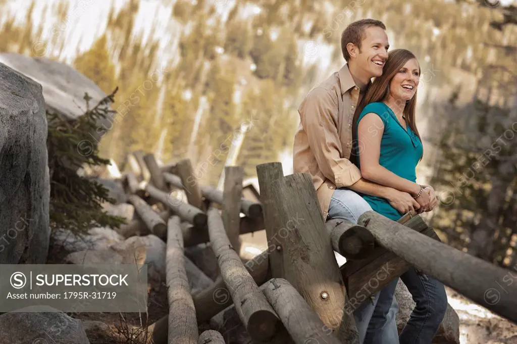 Happy couple sitting on log fence