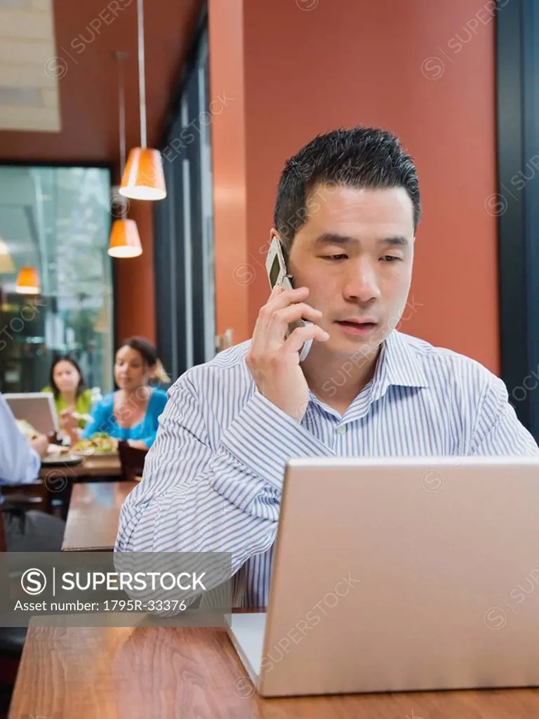Man talking on phone and working on laptop in restaurant