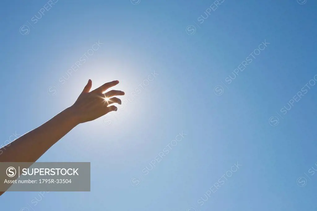Hand in front of a sun flare in the sky