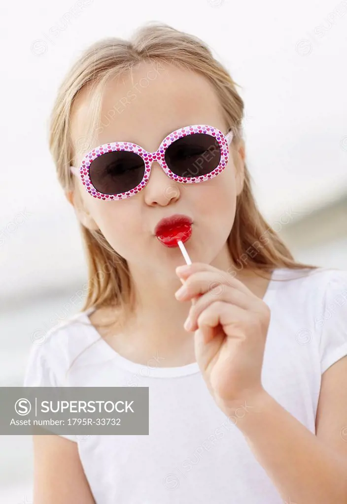 Girl 10_11 wearing sunglasses on beach is licking lollypop