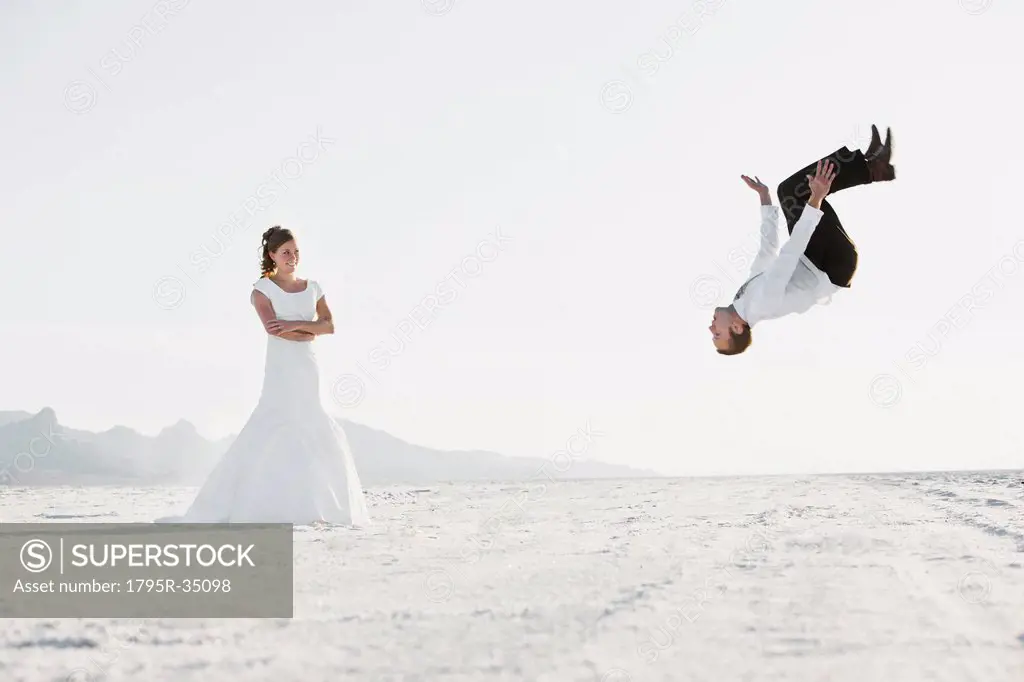 Bride watching groom performing backflip in desert