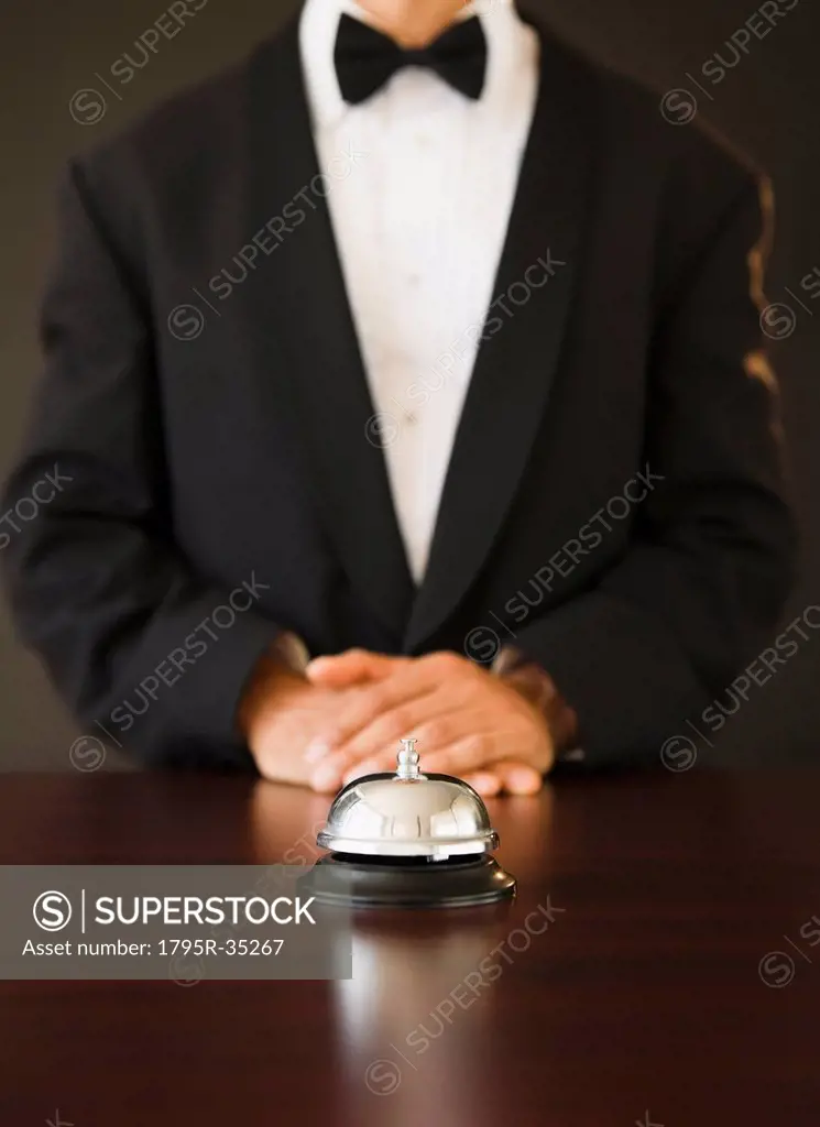 Service bell in the foreground, man wearing bow tie in the background, studio shot