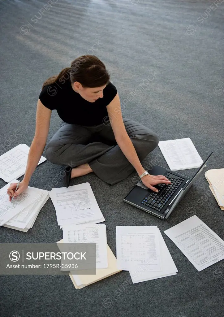 Woman sitting on floor with laptop with documents around