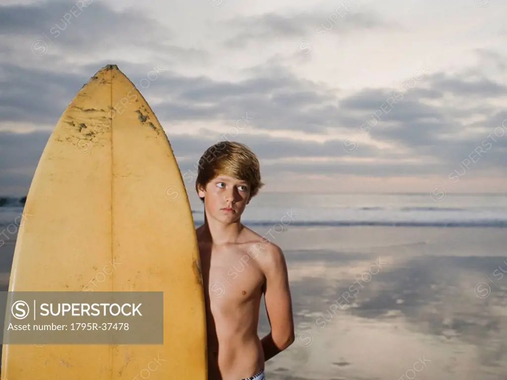 Boy standing beside surfboard