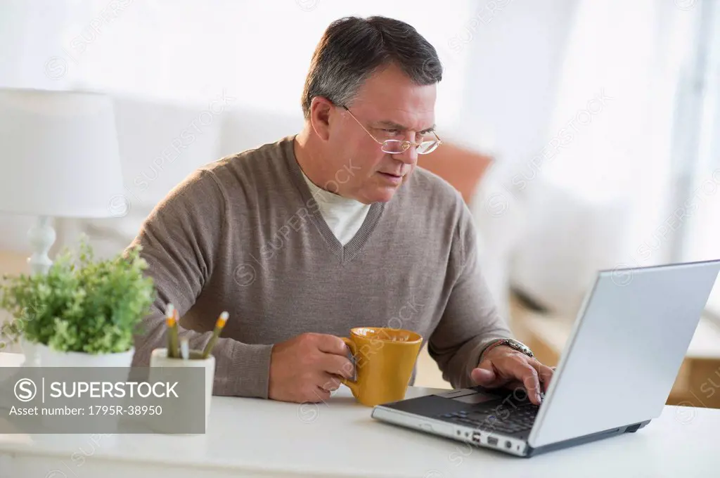 USA, New Jersey, Jersey City, Man using laptop, holding drink in living room
