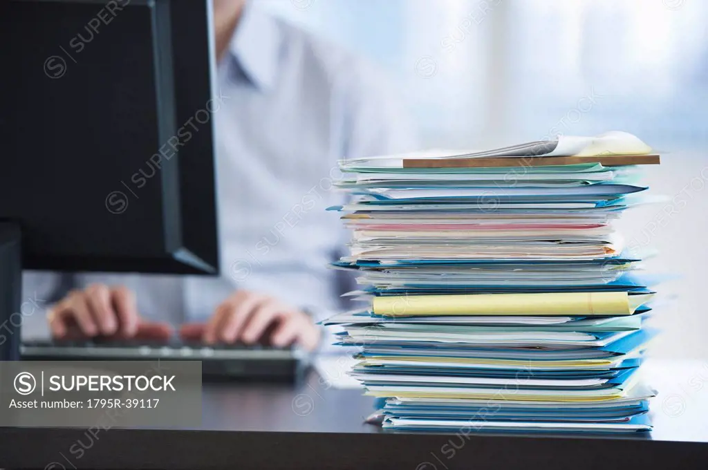USA, New Jersey, Jersey City, Paperwork on desk by businessman using computer