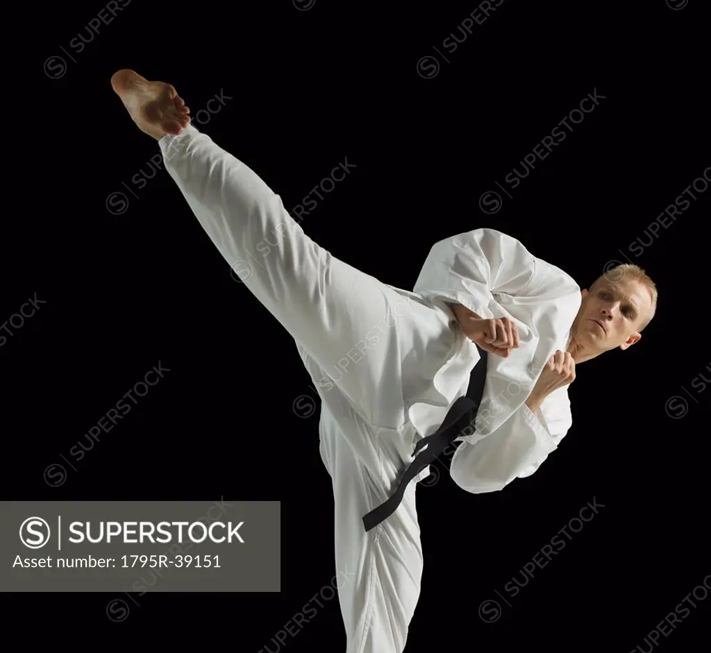 Young man performing karate kick on black background