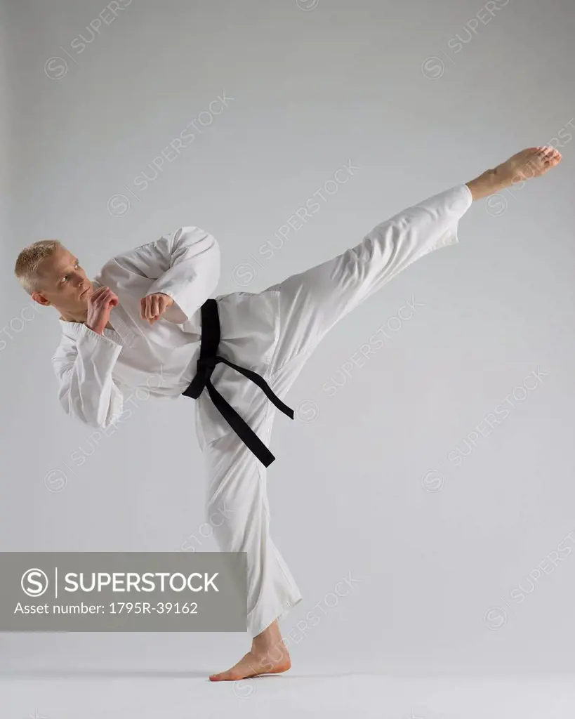 Young man performing karate kick on white background