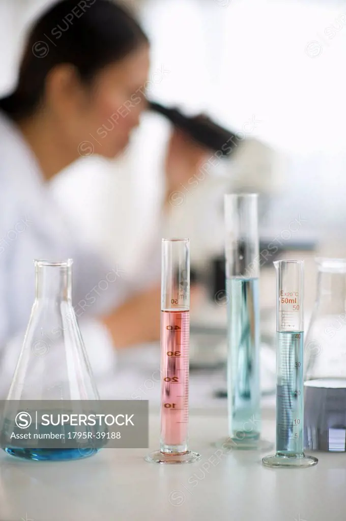 USA, New Jersey, Jersey City, Female scientist using microscope behind test tubes and flasks
