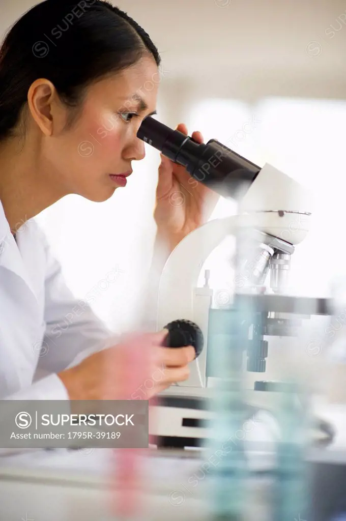 USA, New Jersey, Jersey City, Female scientist using microscope behind test tubes