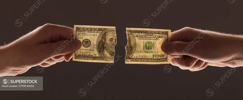 Hands holding torn one hundred dollar bill