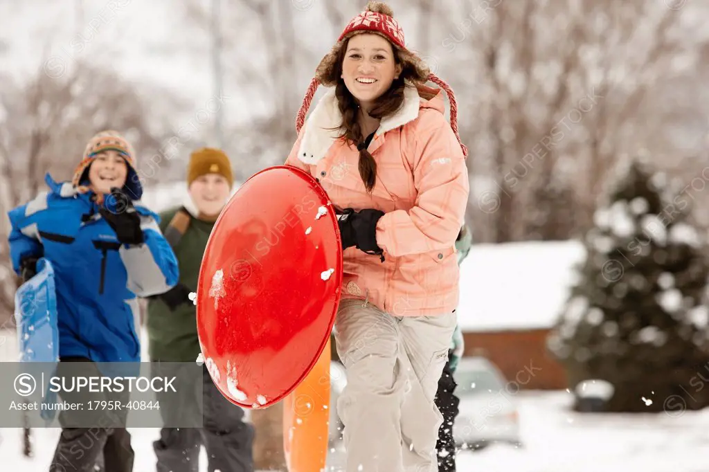 USA, Utah, Provo, Teenage 16_17 girl running with sledge, boys and girls 10_11, 12_13 in background