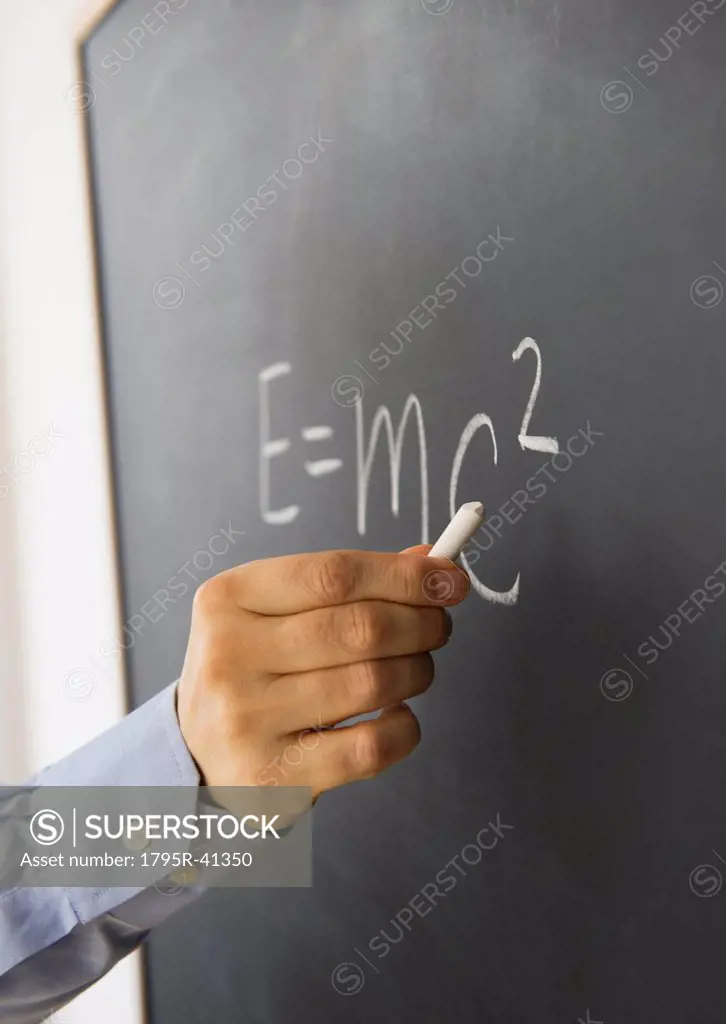 Close_up of man´s hand writing theory of relativity formula on blackboard