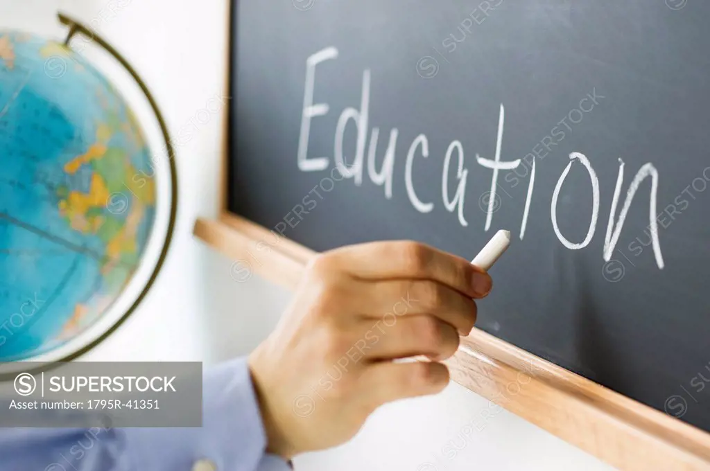 Close_up of man´s hand writing education on blackboard
