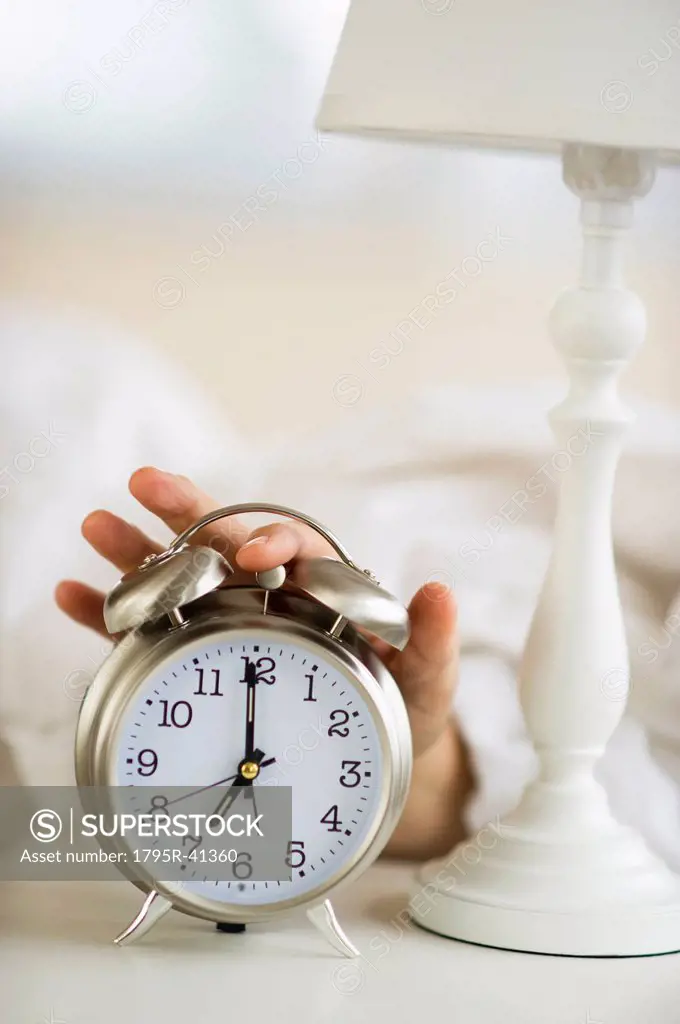 Close_up of man´s hand reaching to alarm clock from bed