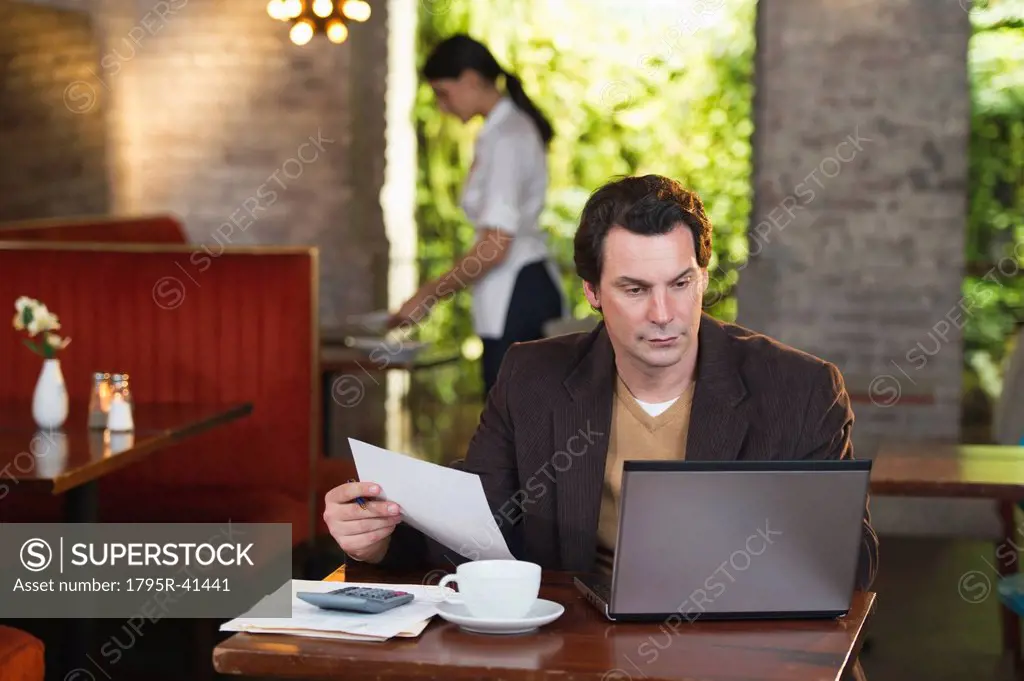 Owner working with laptop in restaurant with waitress in background