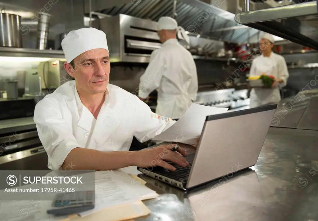Chefs preparing food, one working on laptop