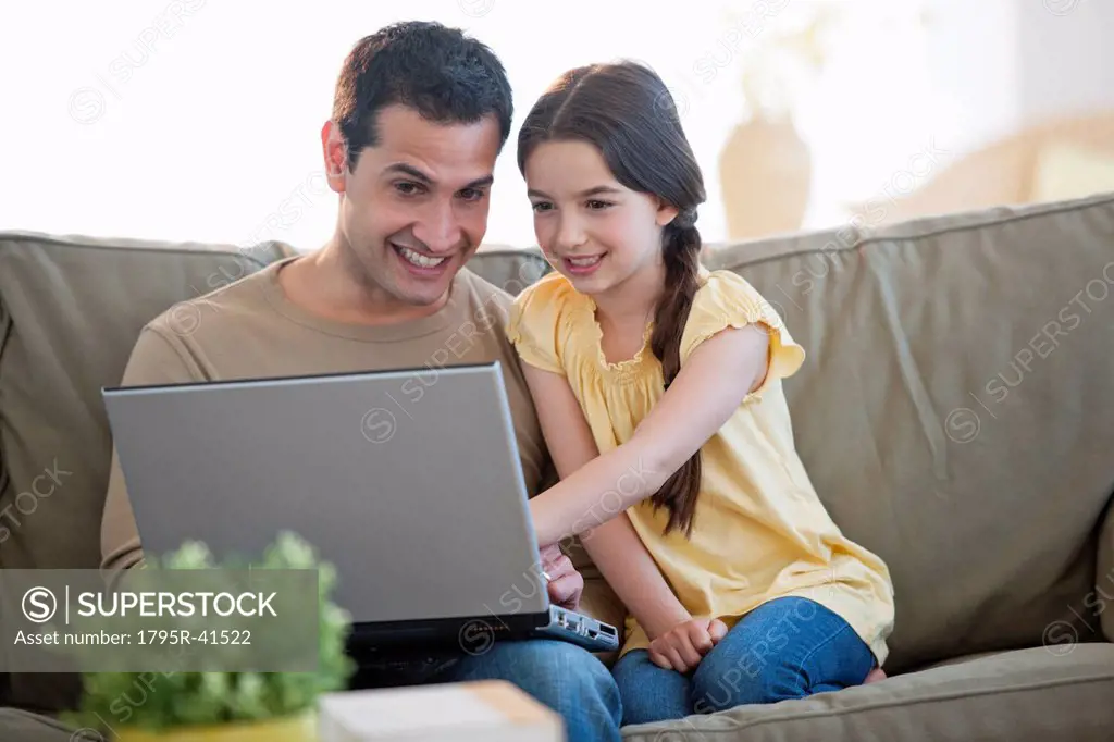 Daughter 8_9 and father sitting on sofa and using laptop