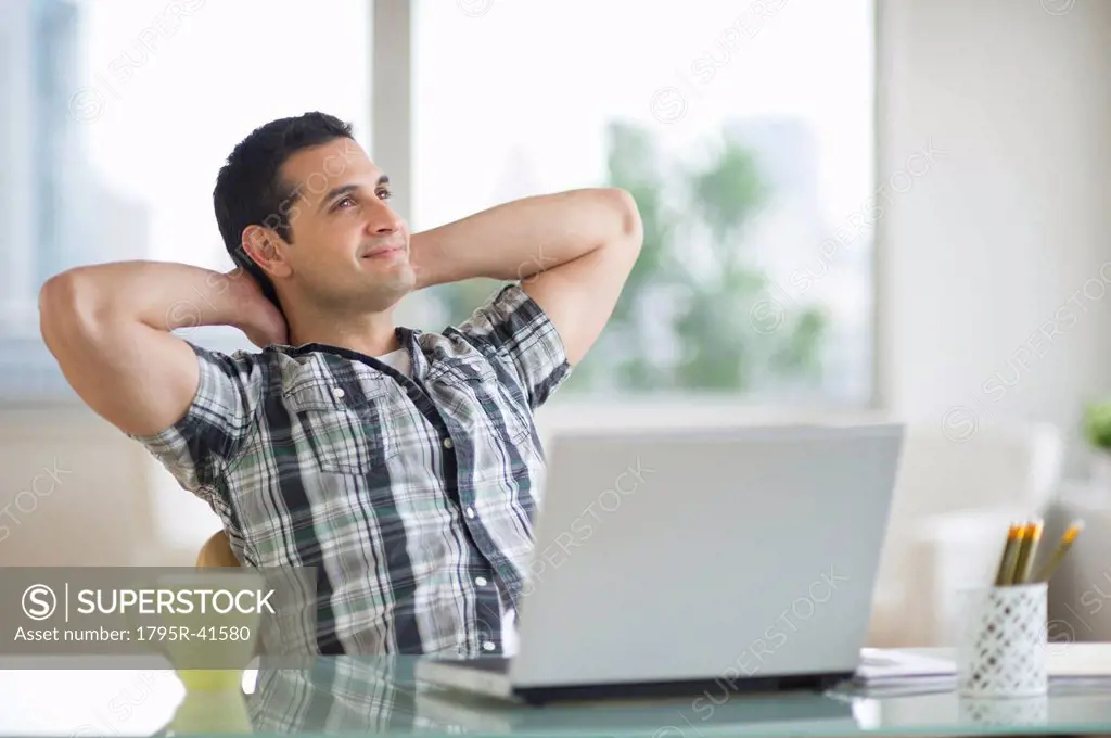 Man sitting at desk with hands behind head