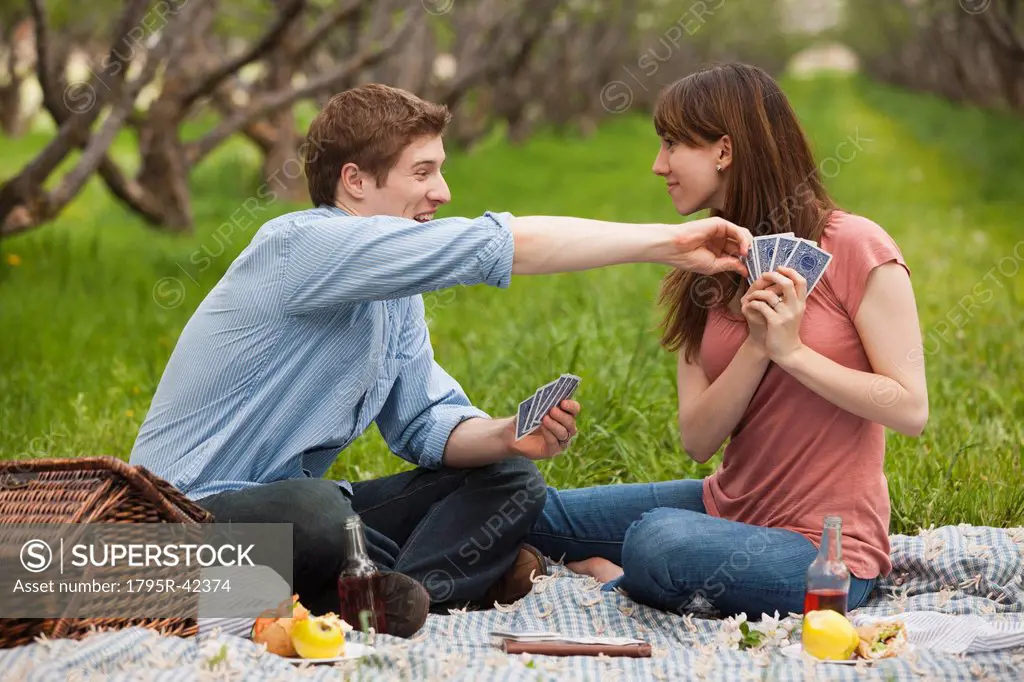 USA, Utah, Provo, Young couple playing cards during picnic in orchard