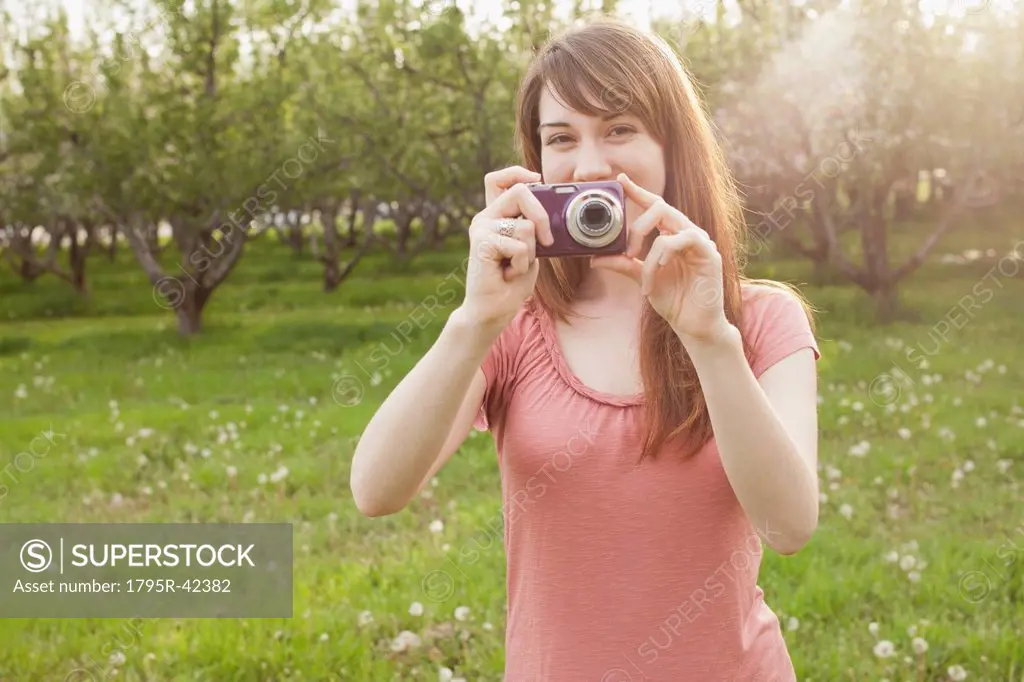 USA, Utah, Provo, Young woman holding digital camera in orchard