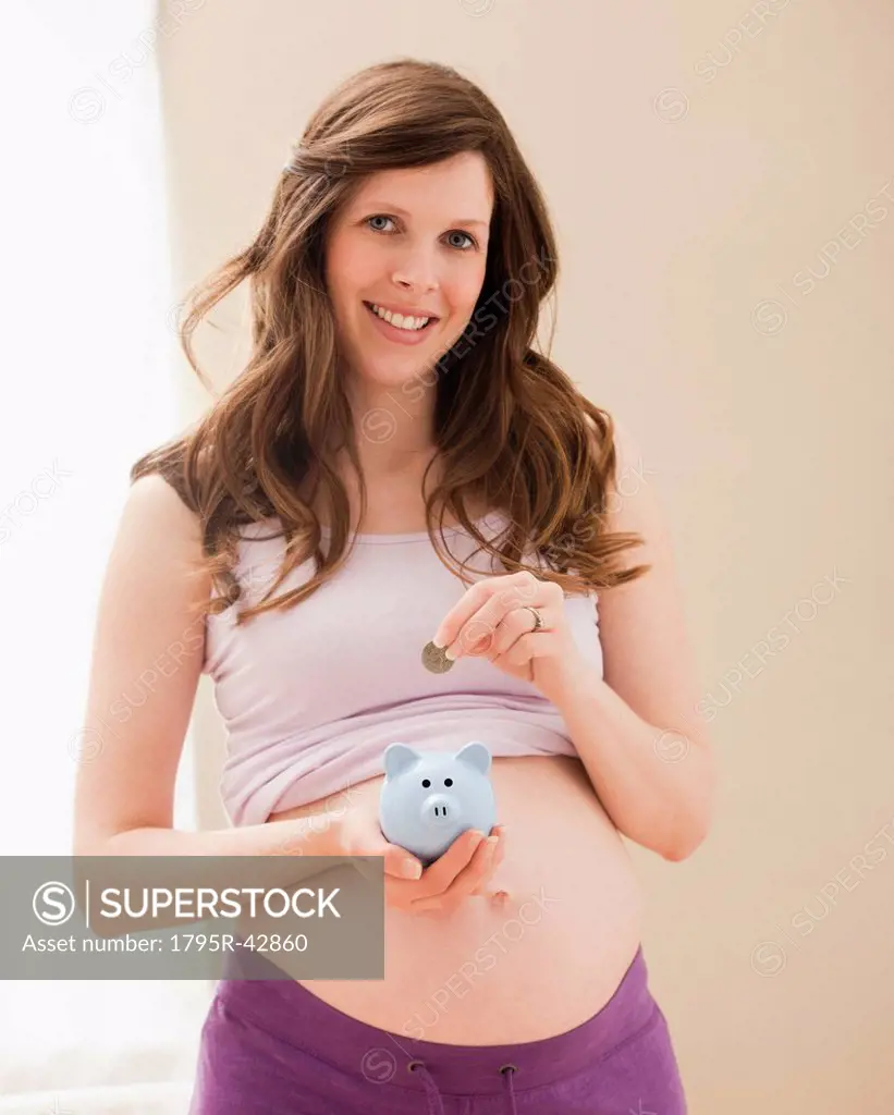 USA, Utah, Lehi, Young pregnant woman putting coin into blue piggybank