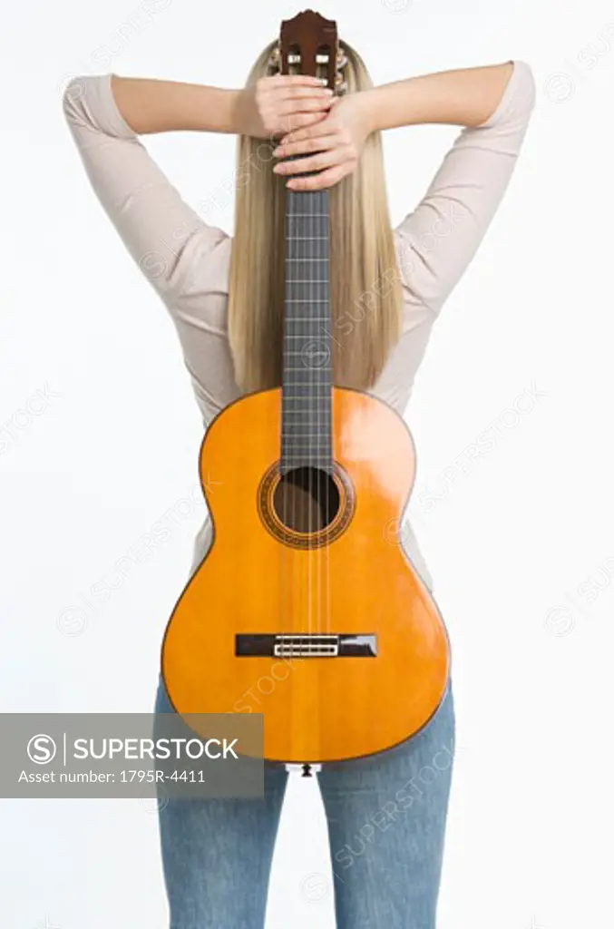 Studio shot of woman holding guitar against her back