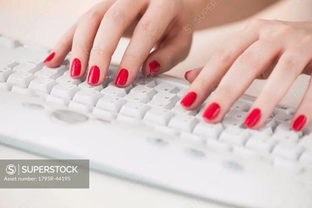 Close up of woman´s fingers with red nail polish typing on computer keyboard