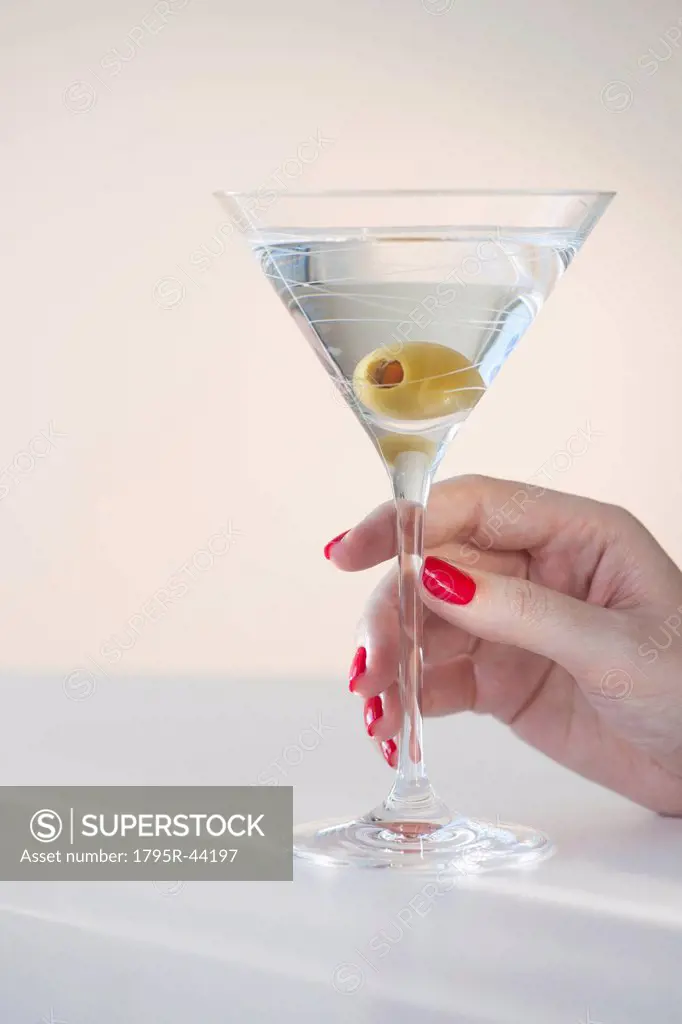 Close up of woman´s hand with nail polish holding martini glass with olive