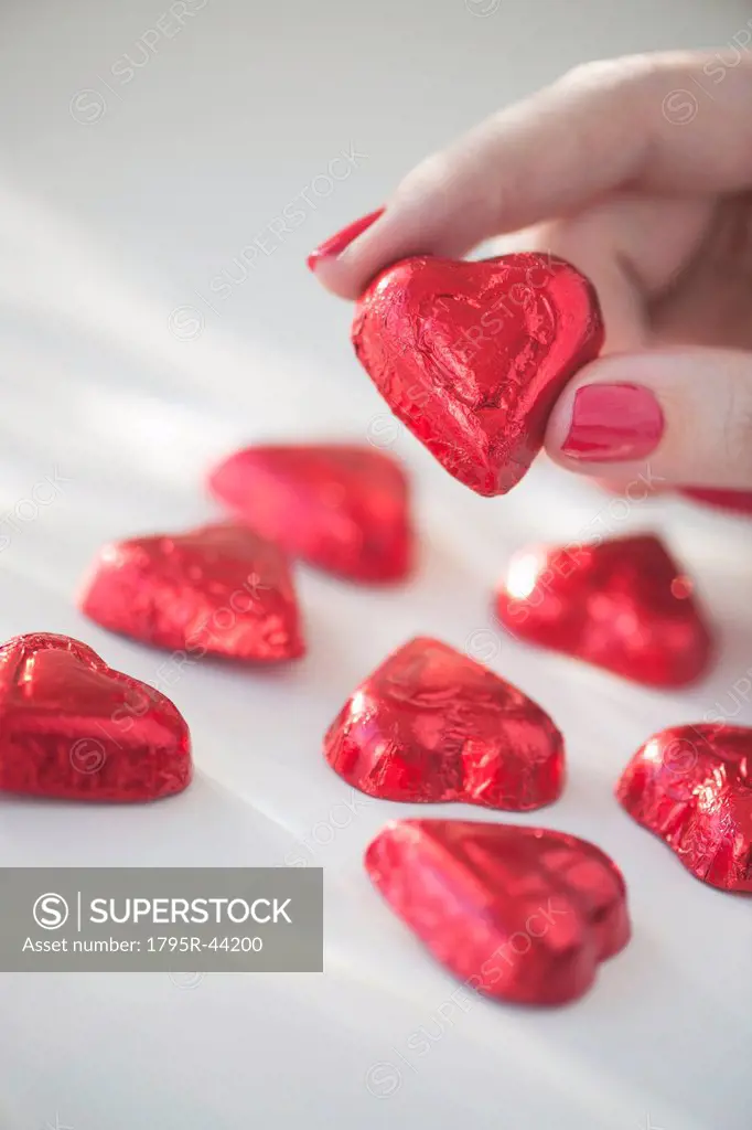 Close up of woman´s fingers with red nail polish holding chocolate in shape of heart in red wrapping
