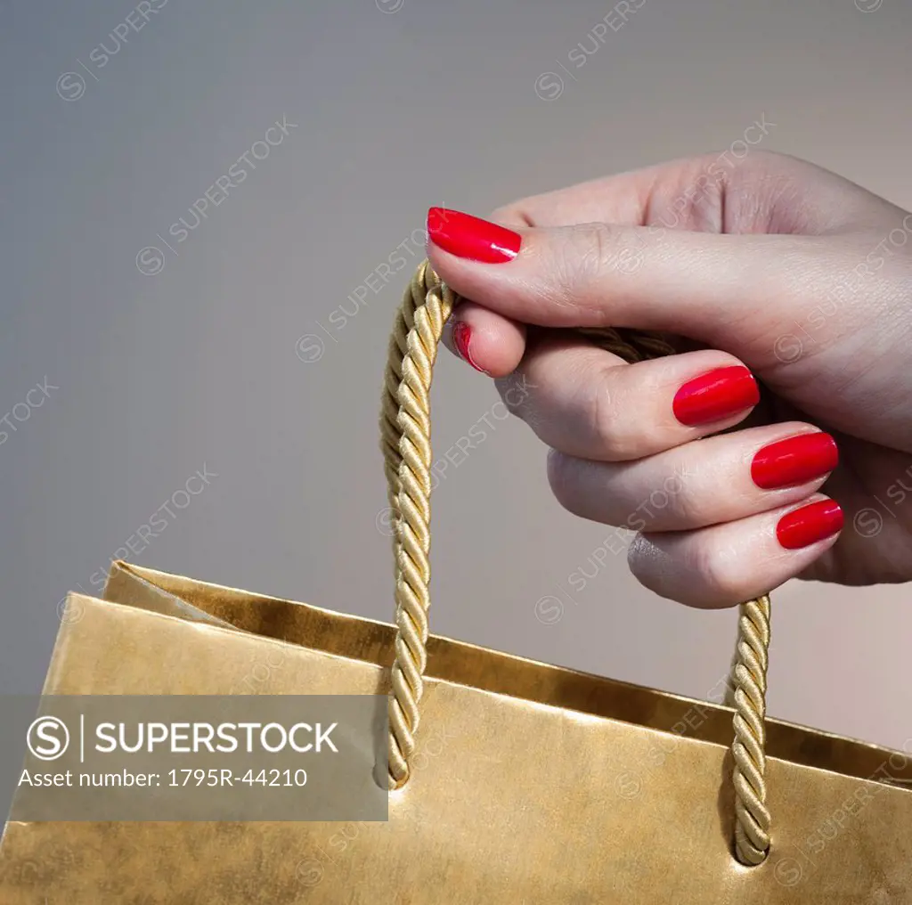 Close up of woman´s hand with red nail polish holding string handle of paper bag