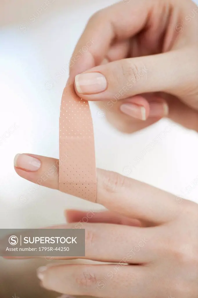 Studio shot of woman sticking adhesive bandage on finger