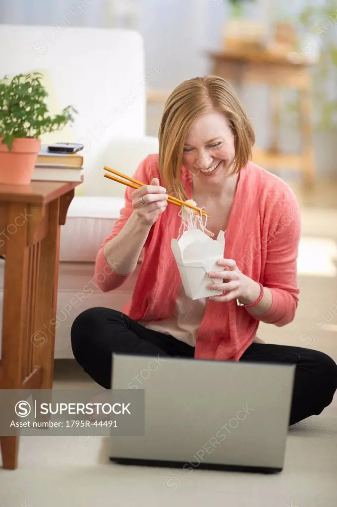 USA, New Jersey, Jersey City, woman sitting on floor, using laptop and eating take out food