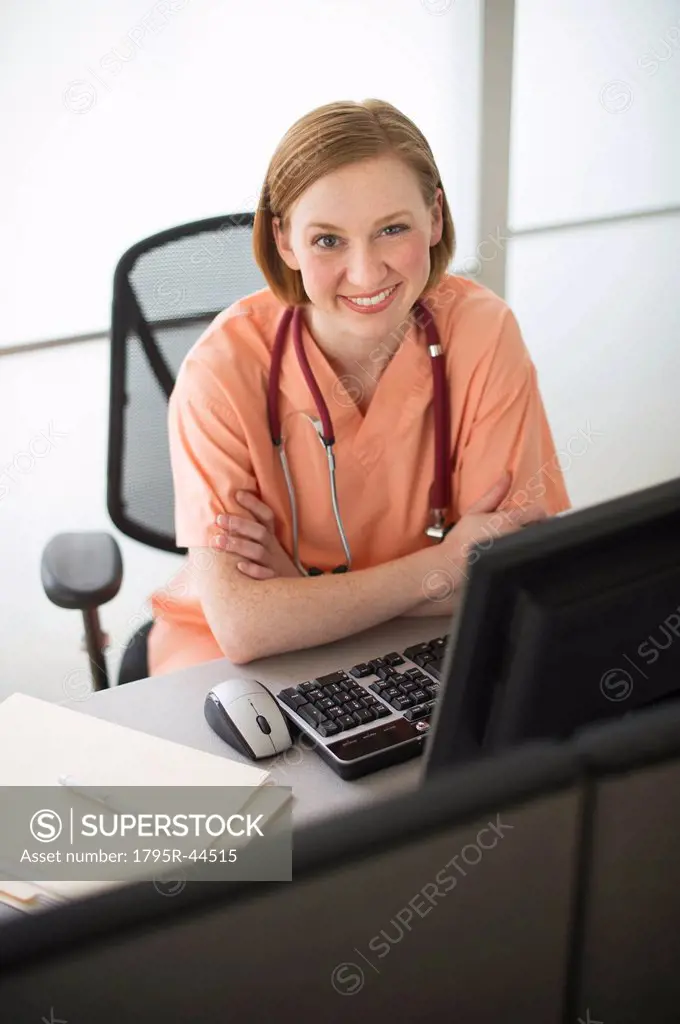USA, New Jersey, Jersey City, female nurse sitting at desk and smiling