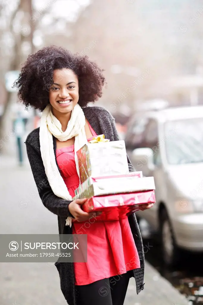 USA, Washington State, Seattle, Young cheerful woman carrying stack of boxed gifts
