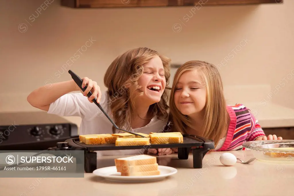 Two girls 10_11 preparing toast in kitchen