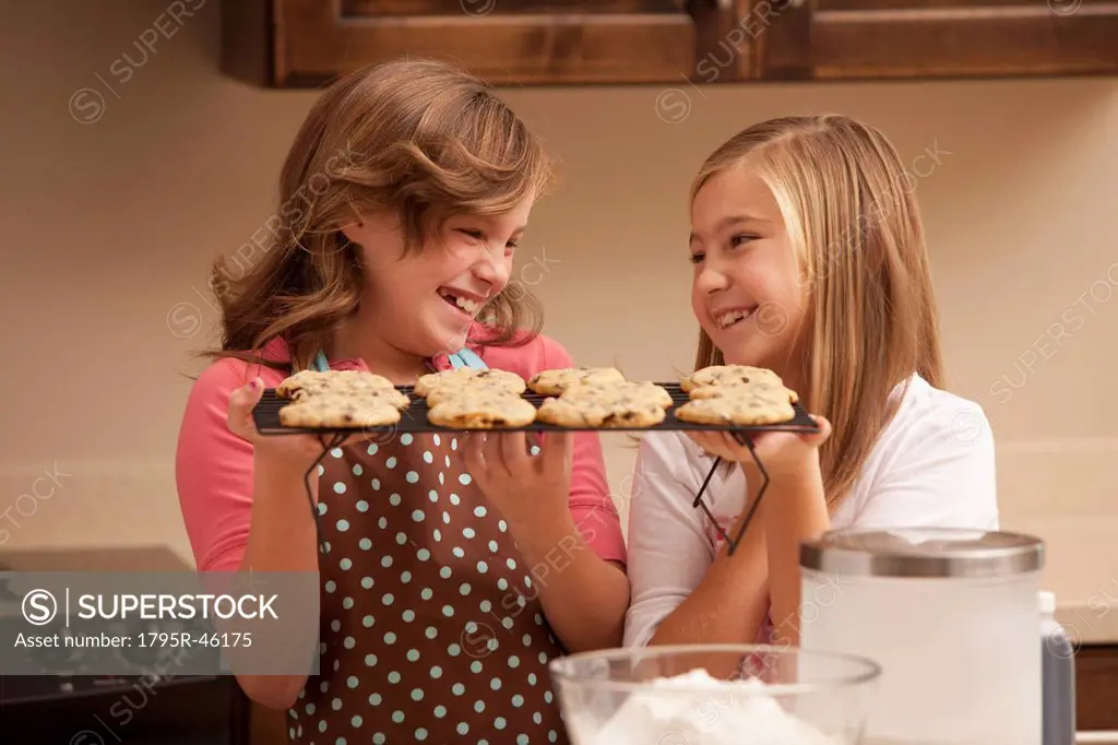 Two girls 10_11 holding biscuits in kitchen