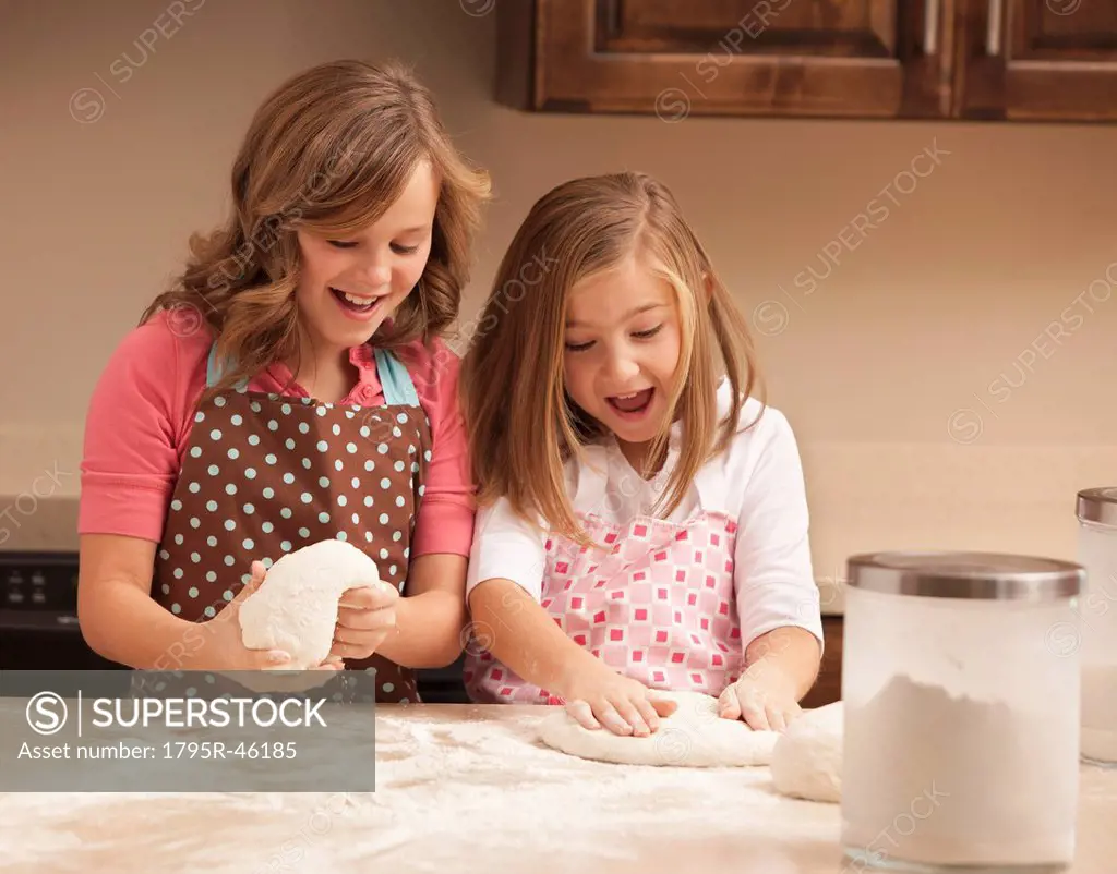 Two girls 10_11 kneading dough in kitchen