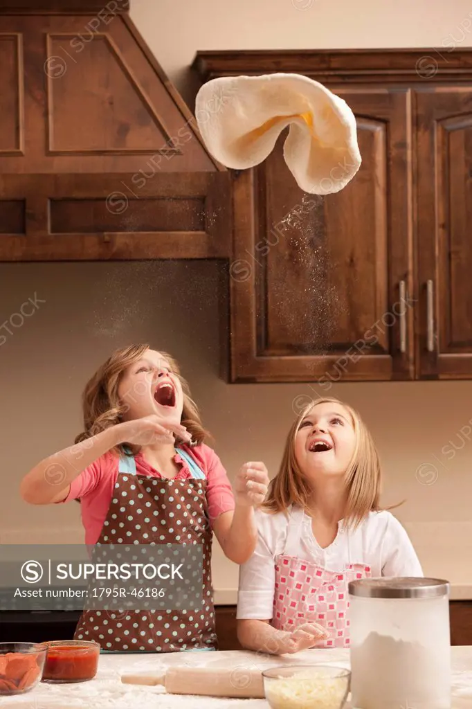 Two girls 10_11 tossing dough in kitchen